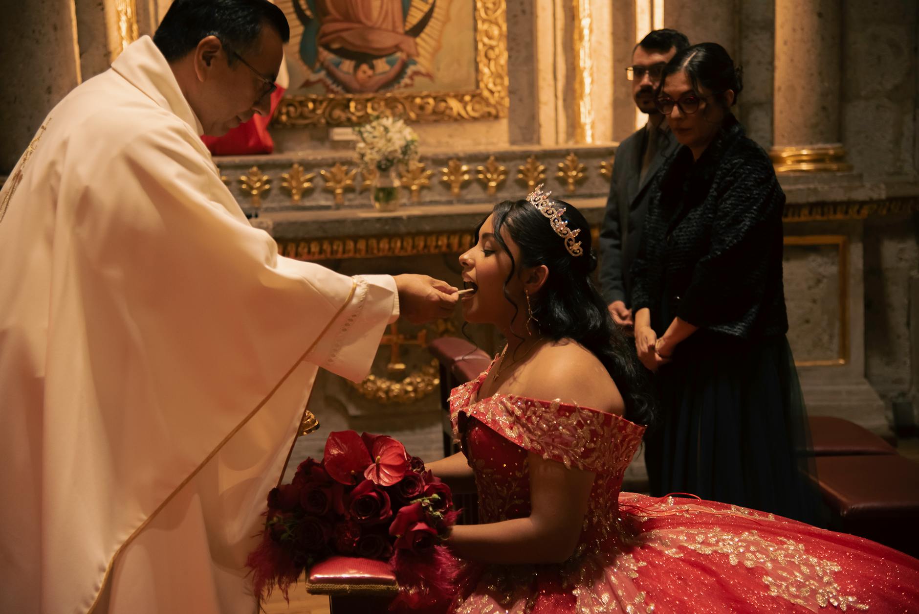 Dziewczyna w czerwonej sukni przyjmuje komunię w ozdobionym kościele