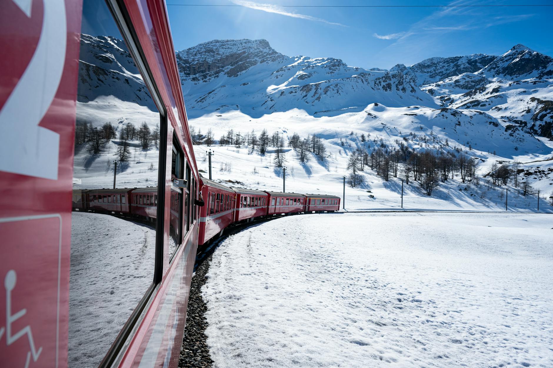 Najpiękniejsze alpejskie trasy kolejowe w Szwajcarii, Niemczech i Austrii: praktyczny przewodnik dla podróżników Czerwony pociąg alpejski jedzie po ośnieżonych zboczach w słoneczny dzień