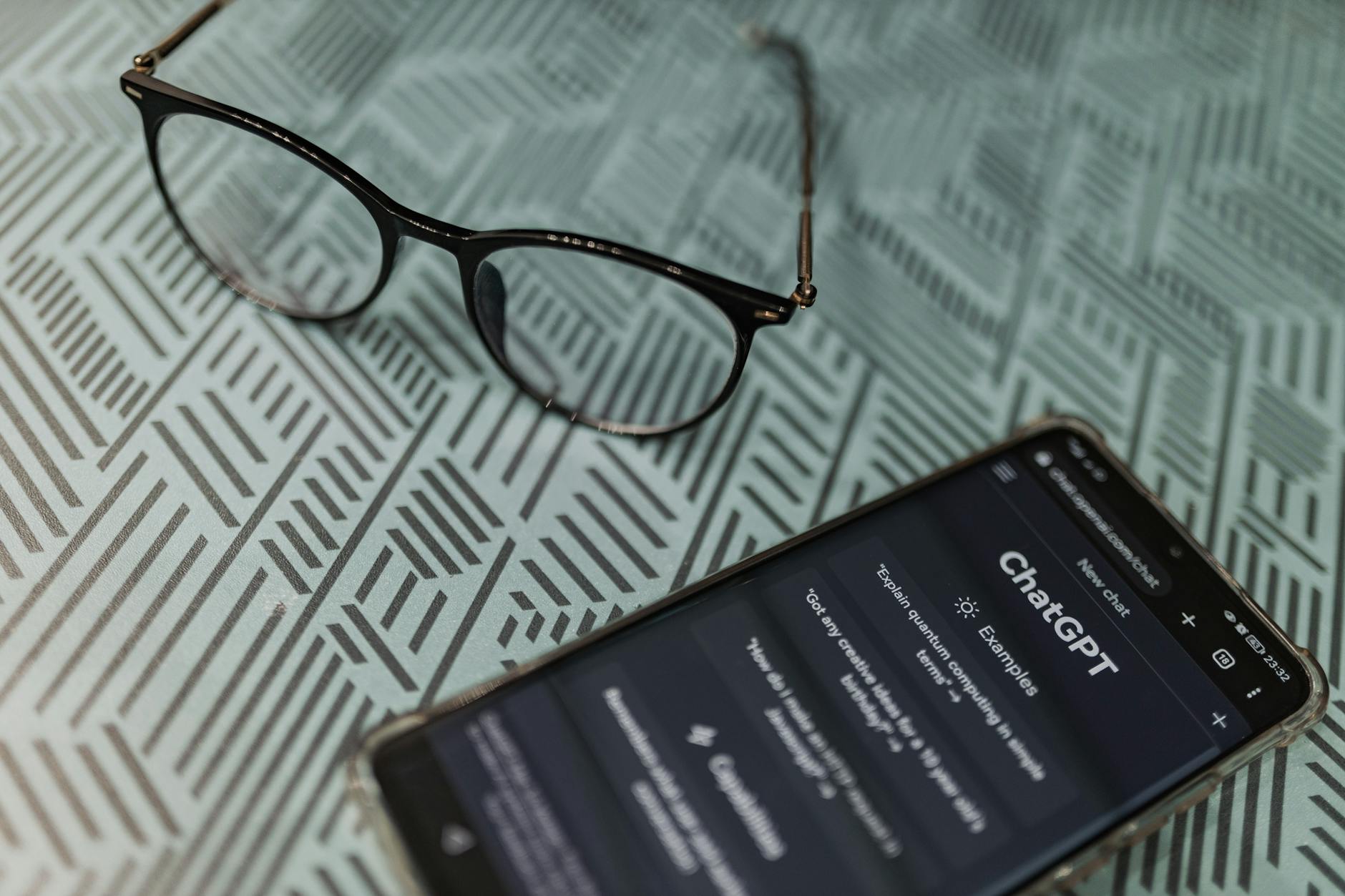 Okulary obok smartfona z włączoną aplikacją ChatGPT na wzorzystym blacie